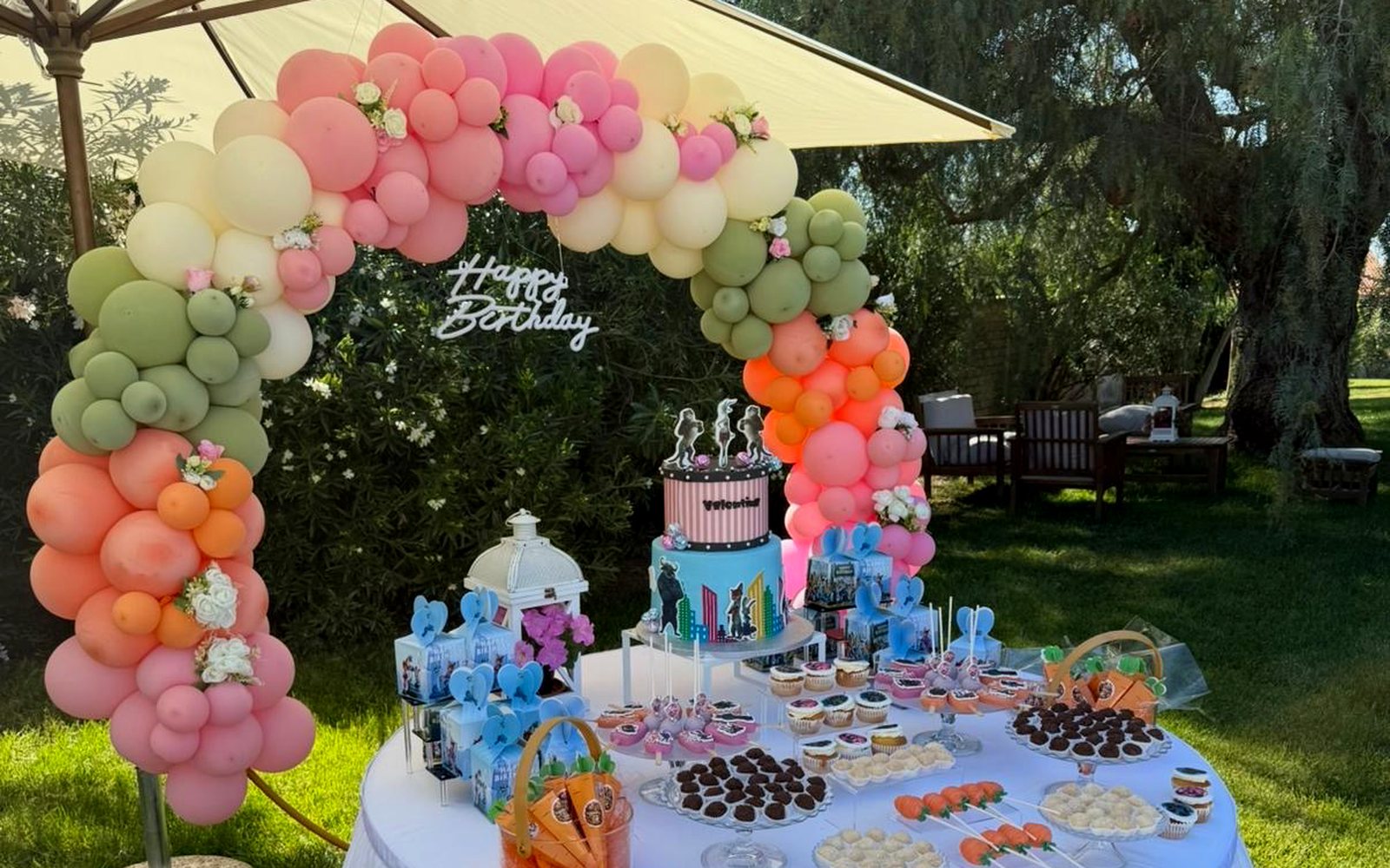 Allestimento compleanno con arco di palloncini e tavolo dolci in giardino